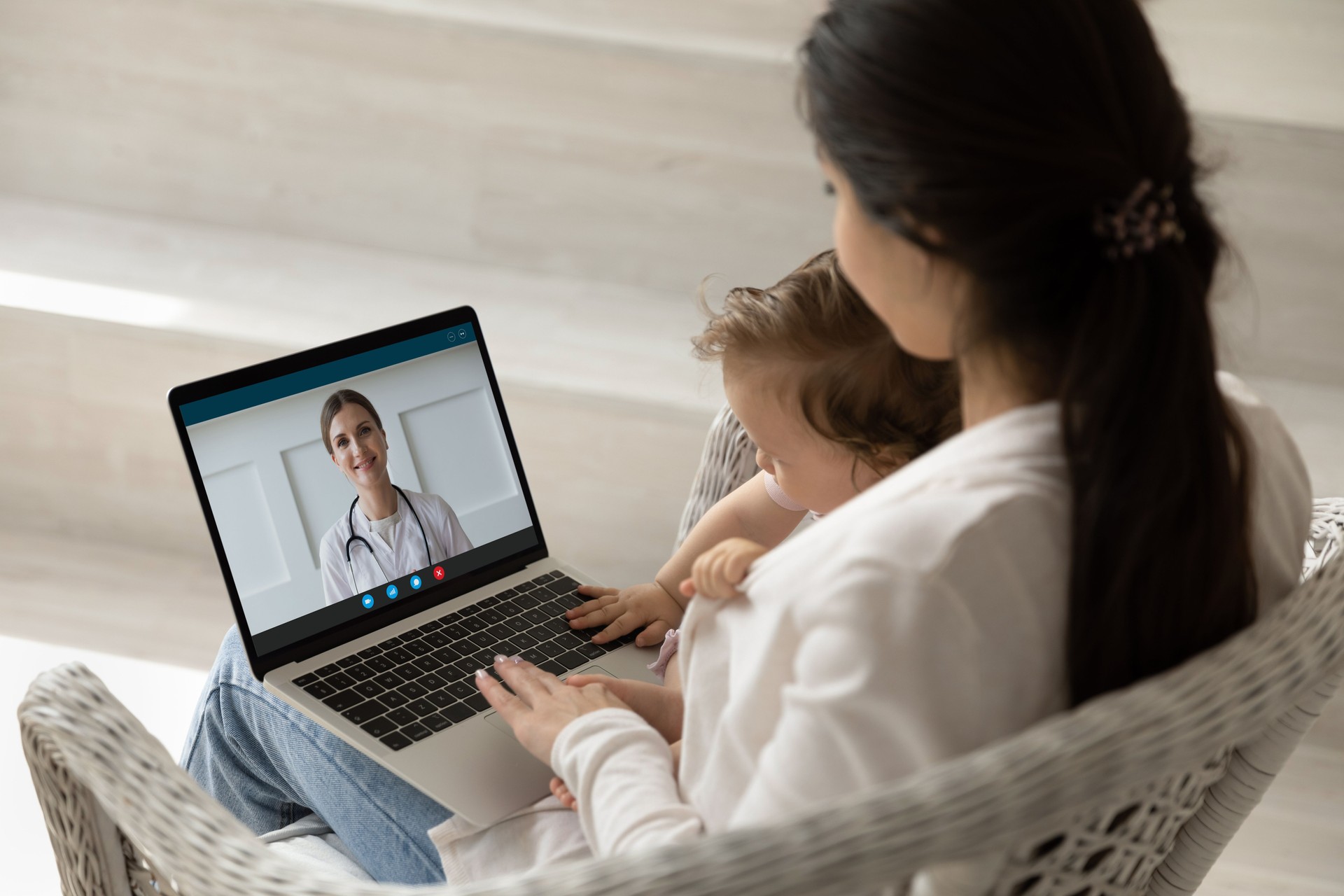 Loving young mother holding baby, making video call to pediatrician