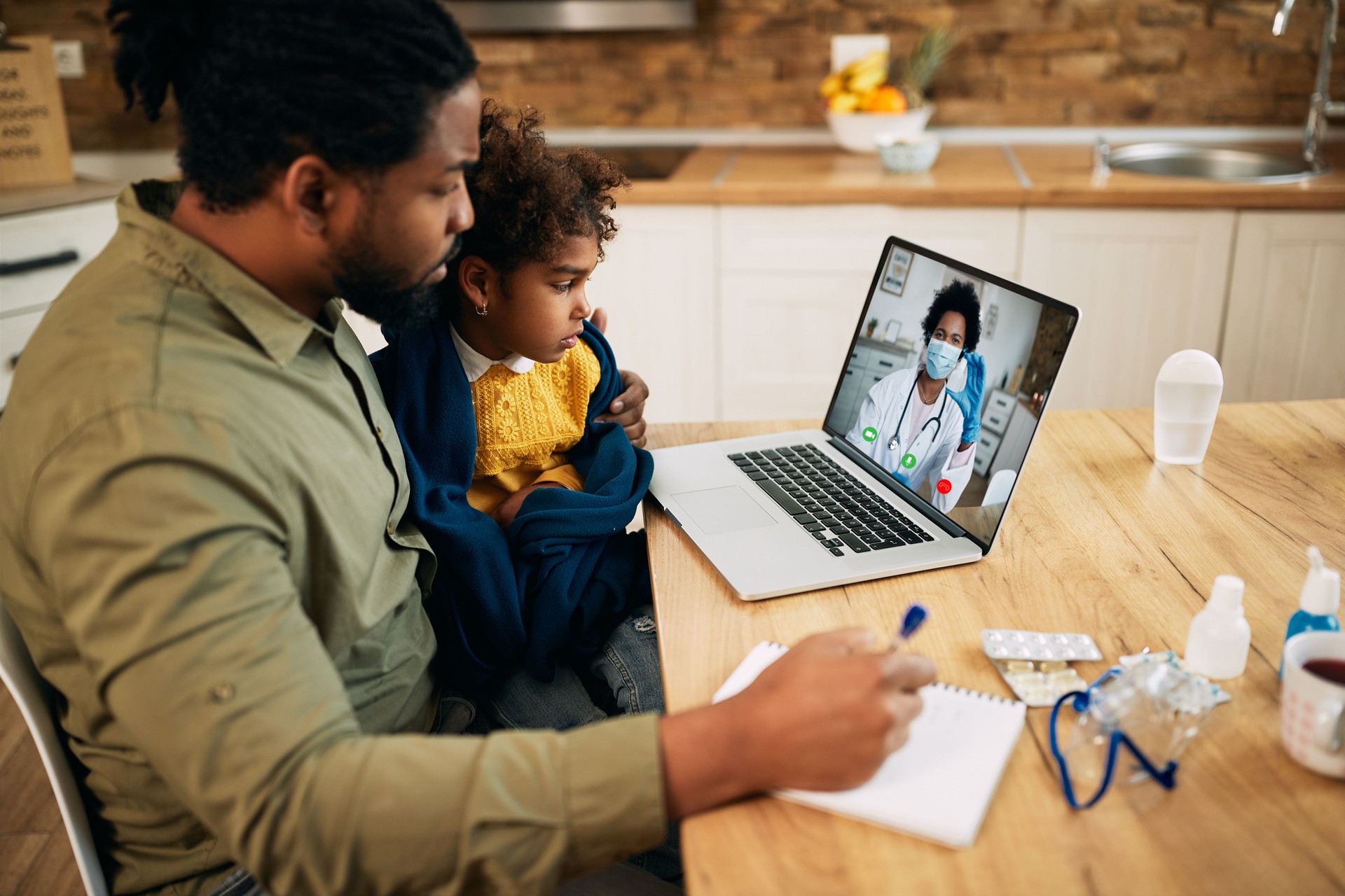 African American father and daughter having video call with family doctor due to coronavirus pandemic.